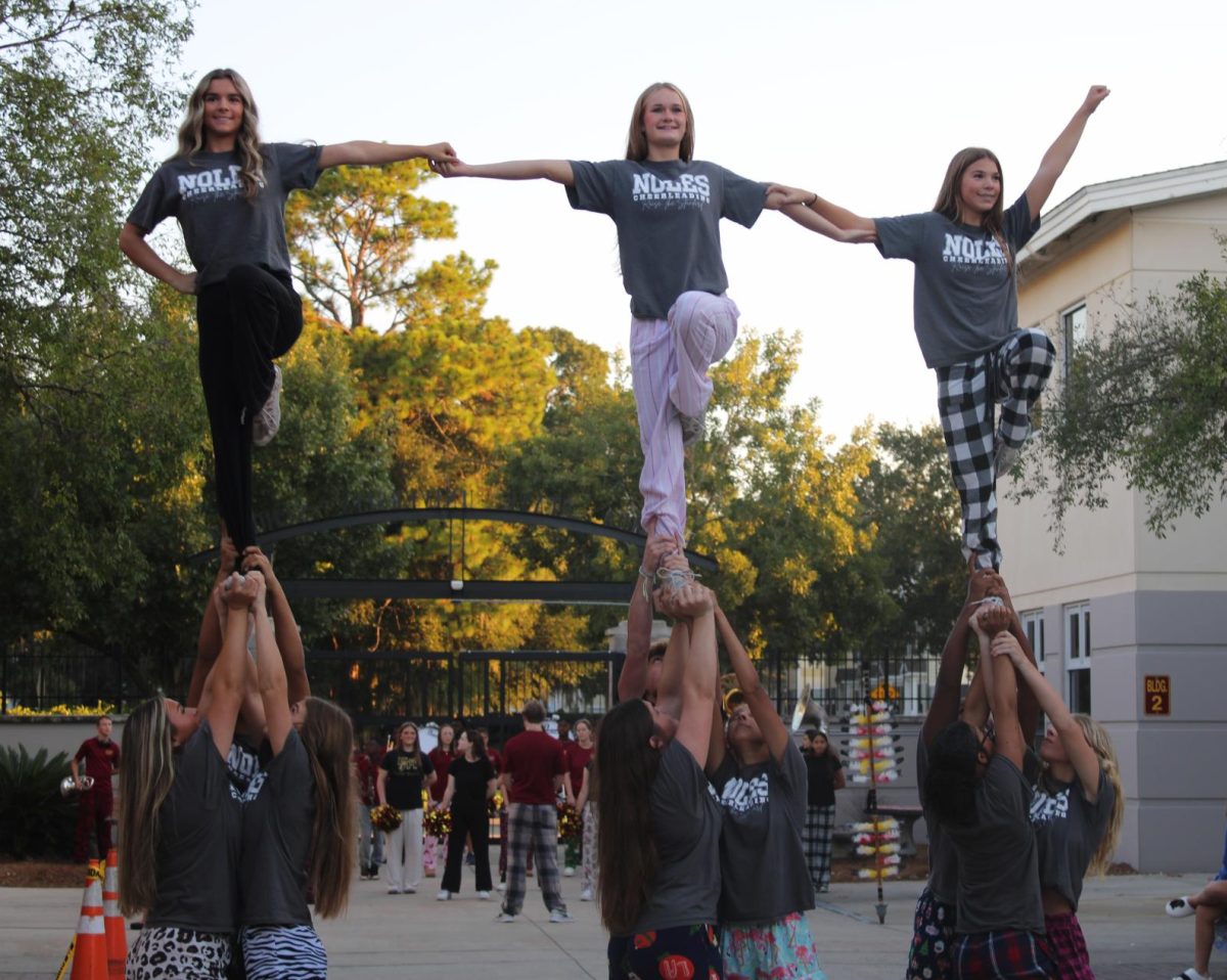 Varsity cheerleaders Hailey Blankenship, Jocelyn Demott and Gabriella Day perform stunts with the careful support of their bases.