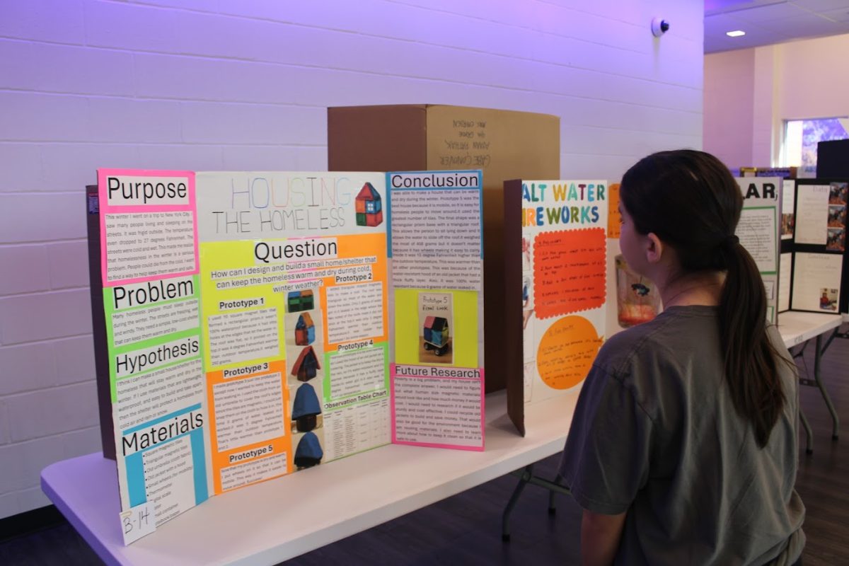 Eighth-grade student Alina Cancel, from science teacher Michael Moran’s class, reads a student’s science project titled “Housing the Homeless”.