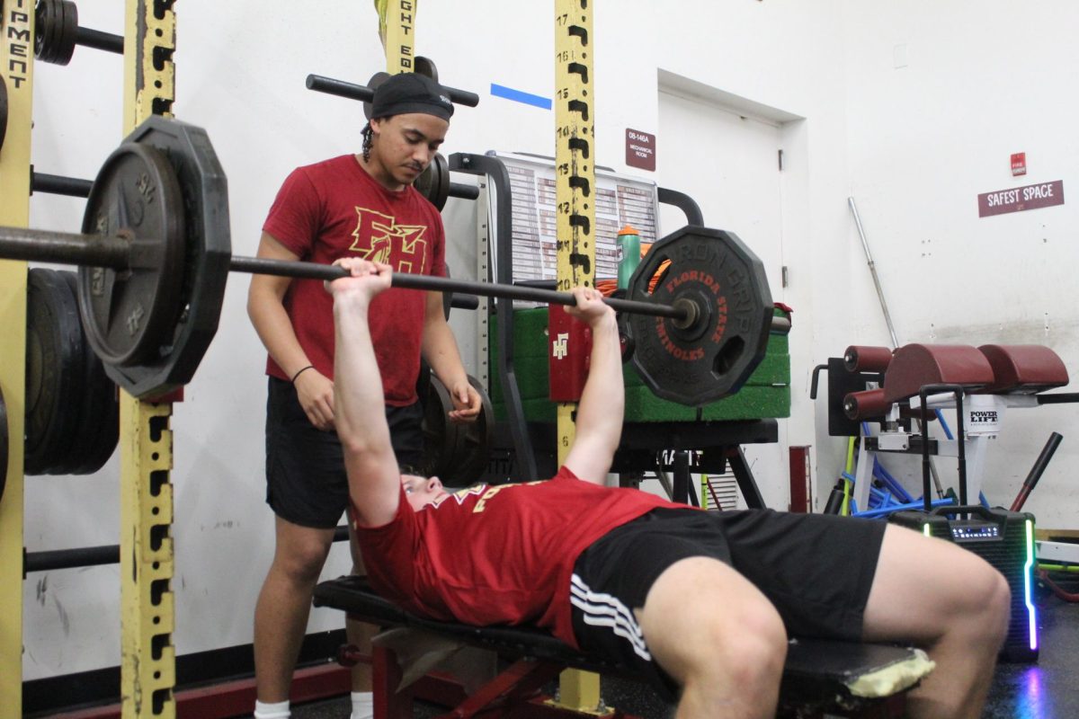 Freshman Zyler Henderson spots for freshman Max Williams during weightlifting practice. The team has just finished districts and is looking toward success at regionals.
Photo courtesy of The Renegade.